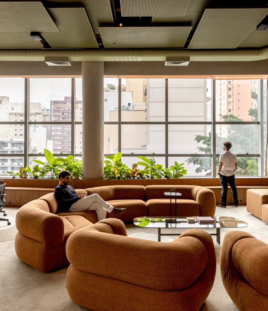 Sofás laranja em volta de uma mesa de centro, com janela e plantas ao fundo